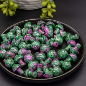 May include: A black plate filled with green and pink gemstone mushroom shaped beads.