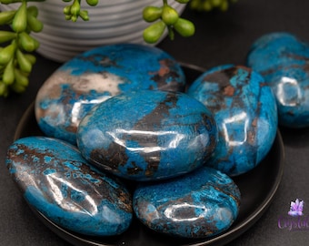 May include: A collection of six blue and black polished stones with a smooth, oval shape. The stones are arranged on a black plate.