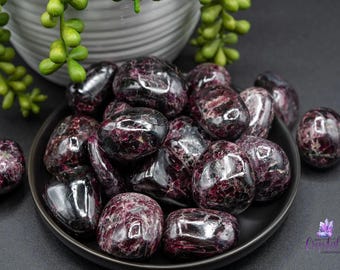 May include: A collection of tumbled red and black gemstones in a black bowl. The stones are smooth and polished, and they have a variety of shapes and sizes.