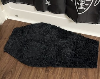 May include: A black bath mat with a textured surface. The mat is shaped like a long oval and has a fuzzy texture.