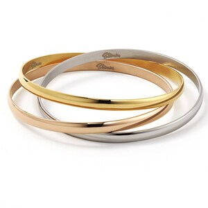 May include: Three interlocking bangle bracelets in silver, rose gold, and gold tones. The bracelets are stacked on top of each other and have a shiny finish.