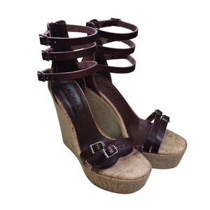 May include: A pair of brown leather wedge sandals with multiple straps and buckles. The sandals have a cork wedge heel and a cork platform.