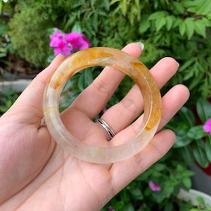 May include: A clear bangle bracelet with a translucent yellow and white pattern. The bracelet is made of natural stone and has a smooth, polished finish.