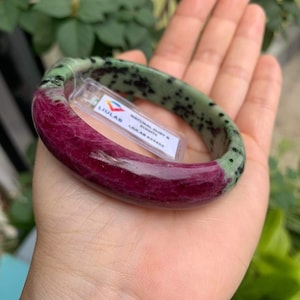 May include: A green and red jade bangle bracelet with black speckles. The bracelet is made of natural ruby and jade. LIULAB NATURAL RUBY & JADE LIULAB 631432