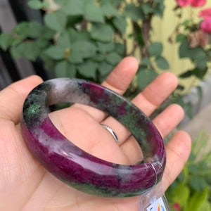 May include: A green and purple gemstone bangle bracelet. The bracelet is made of natural stone and has a polished finish. The bracelet is on a hand, and a tag with the text "LIULAB NATURAL ZODIAC LIUL" is visible.
