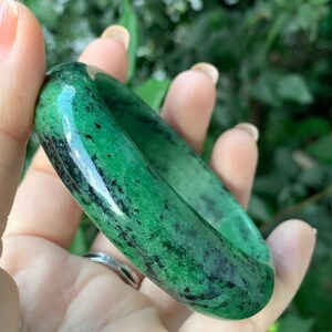 May include: A green jade bangle with black flecks. The bangle is smooth and polished.