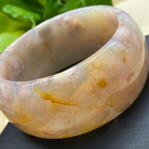 May include: A white agate bangle with brown and orange swirls and patterns. The bangle is smooth and polished.