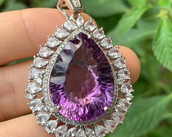 May include: A silver pendant with a large, faceted amethyst gemstone surrounded by a halo of smaller, clear gemstones.