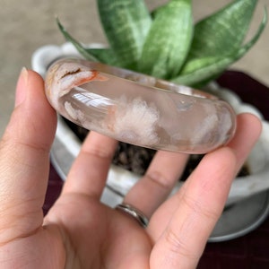 May include: A white agate bangle with a delicate floral pattern. The bangle is translucent and has a light pink hue.