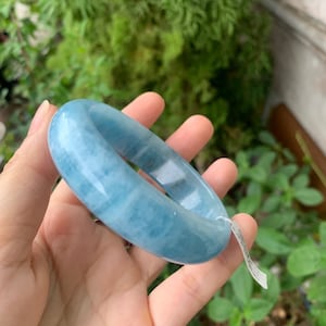 May include: A light blue aquamarine bangle bracelet. The bracelet is smooth and polished, with a slightly cloudy appearance.