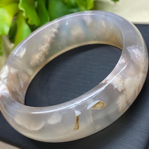 May include: A white agate bangle bracelet with brown and white inclusions. The bracelet is smooth and polished.