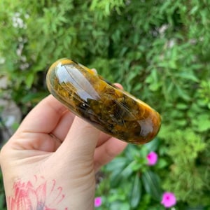 May include: A polished, yellow and green agate bangle bracelet. The bracelet has a smooth, rounded surface and a natural, organic pattern.