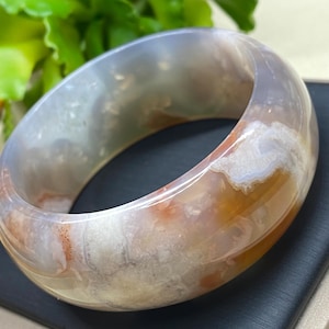 May include: A light brown agate bangle bracelet with white and gray swirls. The bracelet is smooth and polished.