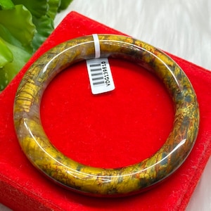May include: A gold and brown bangle bracelet with a marbled pattern. The bracelet is on a red velvet background. The barcode sticker on the bracelet reads "VDG13810".