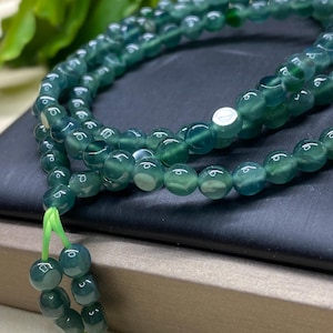 May include: A green jade beaded necklace with a green tassel. The necklace is made of round beads and is strung on a green cord.
