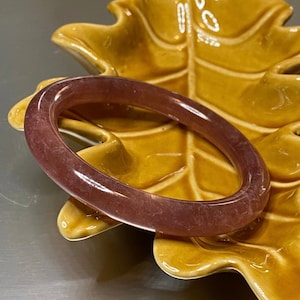 May include: A purple jade bangle bracelet resting on a ceramic leaf-shaped dish.