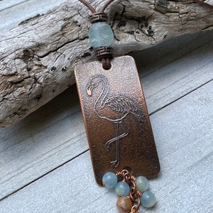 May include: A copper pendant necklace with a flamingo design and a beaded tassel. The beads are a mix of light blue and brown.