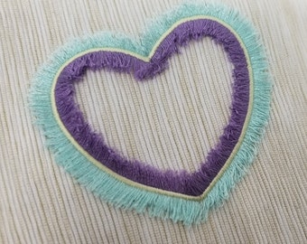 May include: A heart-shaped design with a light blue fringe and a purple inner border on a white textured background.