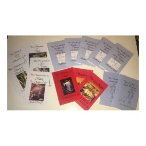May include: A collection of 12 small, colorful books with illustrations and titles related to the Bible. The books are arranged in two rows on a light brown surface. The titles include "The Birth of Jesus", "The Adoration of the Magi", "The Visitation of Mary to Elizabeth", "The Presentation of Jesus in the Temple", "The Annunciation to Mary", "The Parable of the Kingdom of Heaven and the Yew", "The Parable of the Kingdom of Heaven and the Mustard Seed", "The Parable of the Kingdom of Heaven and the Hidden Treasure", "The Women at the Tomb", "Pentecost", "The Last Supper", "The Parable of the Lost Sheep", and "The Parable of the Good Shepherd".
