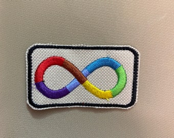 Puede incluir: Un parche blanco bordado con un símbolo de infinito de color arcoíris. El parche tiene un borde negro.