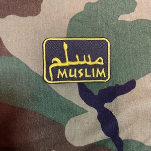 Könnte beinhalten: Ein gestickter Aufnäher in Schwarz und Gold mit dem Wort "MUSLIM" und dem arabischen Wort für "Muslim" in goldener Farbe.