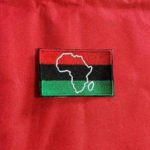 May include: A red, black and green fabric patch with a white outline of the continent of Africa.