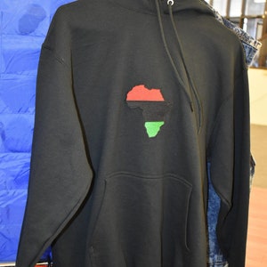 Puede incluir: Sudadera con capucha negra con un contorno rojo, negro y verde del continente africano en la parte delantera.