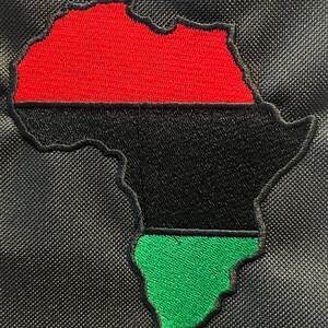 May include: Embroidered patch depicting the African continent in red, black, and green. The patch is sewn onto black fabric with a textured finish. The design is a stylized representation of the African continent.