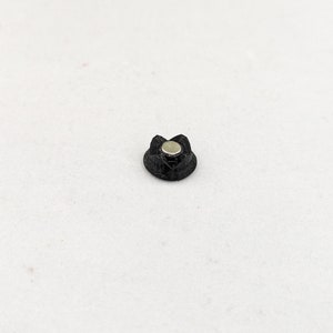 May include: A black plastic flower-shaped object with a silver metal center.