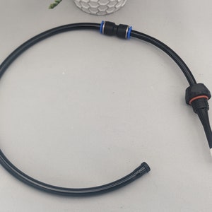 以下が含まれることがあります： 一方の端に黒いコネクタ、もう一方の端に白い先端が付いた黒い柔軟なチューブ。チューブは巻かれており、コネクタに青いリングが付いています。
