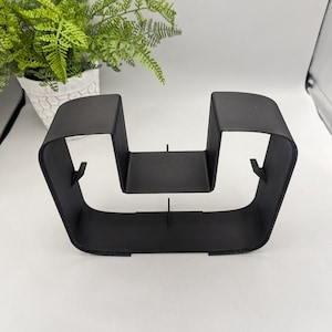 May include: A black metal stand with two vertical supports and a horizontal shelf. The stand is designed to hold two items, such as glasses or mugs.