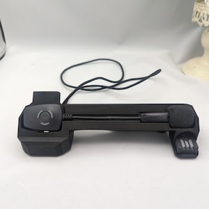 May include: A black headset stand with a microphone and a control button. The stand has a cord attached to it.