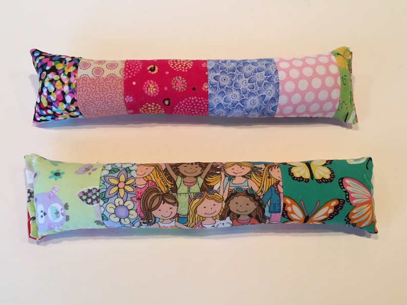 May include: Two colorful fabric pillows with different patterns. The top pillow has a patchwork design with pink, red, blue, and white fabrics. The bottom pillow has a green fabric with a butterfly pattern and a fabric with a pattern of girls.