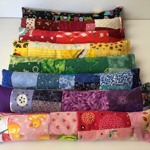 May include: A stack of colorful patchwork fabric pillows, each with a different pattern. The pillows are arranged in a rainbow order, from red to purple. The pillows are all rectangular and have a soft, quilted texture.
