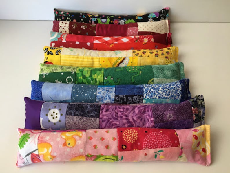 May include: A stack of colorful patchwork fabric pillows, each with a different pattern. The pillows are arranged in a rainbow order, from red to purple. The pillows are all rectangular and have a soft, quilted texture.
