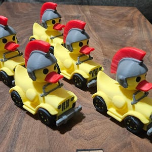 May include: Six yellow toy duck figures, each in a small jeep-like vehicle. The ducks wear gray helmets with red crests and have red beaks. The vehicles have black wheels and gray bumpers, arranged on a wooden surface.
