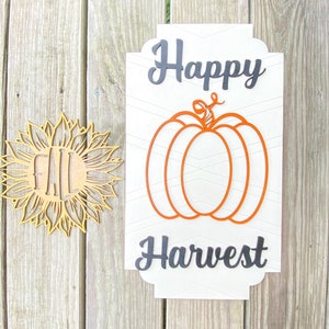 Peut inclure: Une pancarte en bois blanc avec une inscription noire qui dit "Happy Harvest". La pancarte présente une grande citrouille orange avec une tige et un motif en chevron.