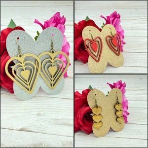 May include: Three pairs of heart-shaped earrings. The first pair is gold with a layered heart design. The second pair is red with a layered heart design. The third pair is gold with three small hearts hanging from a larger heart.