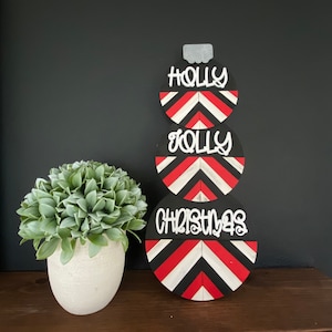 May include: A three-tiered Christmas ornament decoration with a black background and red and white chevron stripes. The top tier says "HOLLY", the middle tier says "JOLLY", and the bottom tier says "CHRISTMAS".