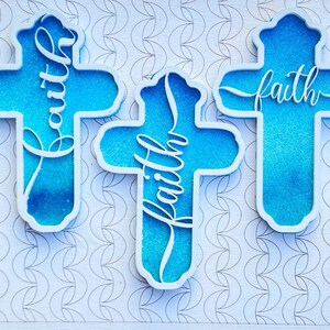 May include: Three white wooden crosses with a blue glitter background. Each cross has the word "faith" written in white cursive.
