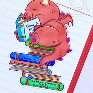 May include: A red dragon with a book titled "How to Fly" is sitting on a stack of books. The books are titled "Arago", "Flame Grilling", and "Better Homes and Hoards".