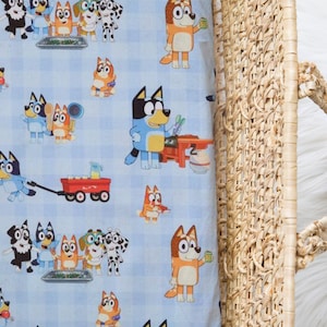 Puede incluir: Una tela azul claro con un patrón repetido de perros de dibujos animados en varias poses. Una cesta tejida con asa está en el lado derecho de la imagen. La tela tiene un patrón de cuadros.