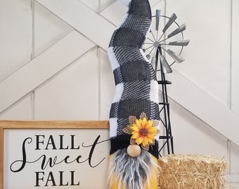 Peut inclure: Un gnome jaune avec un chapeau en plaid buffalo noir et blanc et un tournesol. Le gnome est debout sur une surface en bois avec une pancarte qui dit "Fall Sweet Fall".
