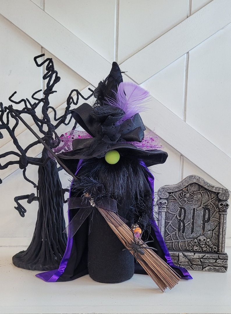 Peut inclure: Un gnome de sorci&egrave;re noir portant un chapeau violet, une cape noire et tenant un balai. Le gnome a un nez vert et se tient devant une pierre tombale sur laquelle est inscrit "RIP".