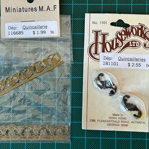 May include: Two packs of miniature decorative trim. The first pack contains two gold metal trims with floral designs. The second pack contains two black metal scorpions. The packs are labelled with the name "Houseworks LTD" and the price of £2.55.