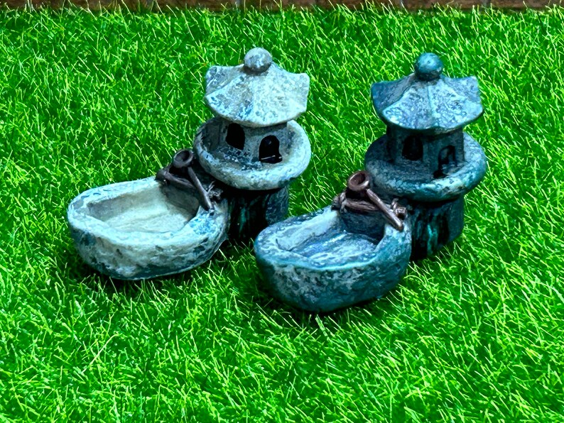 May include: Two miniature gray stone pagodas with small bowls on top, set on a green artificial grass surface.