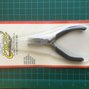 Peut inclure: Une pince à bec plat de 12,7 cm avec des poignées noires, emballée sur une carte blanche et rouge avec le nom de la marque "Excel" et le texte "Our Edge Makes The Difference".