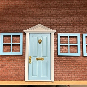 Peut inclure: Une porte d'entrée bleu clair avec une garniture blanche et un heurtoir de porte doré. Il y a quatre fenêtres bleu clair avec une garniture blanche de chaque côté de la porte.