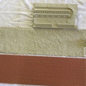 May include: Three textured rubber stamps for creating brick, stone, and cobblestone patterns. The stamps are beige and brown.