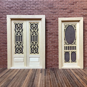 May include: Two miniature wooden doors are displayed against a brick wall. One is a double door with an ornate, swirling design. The other is a single door with an oval screen and a rectangular design below. The doors are light-coloured wood.